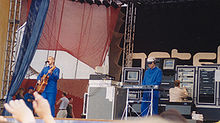 Photo de deux hommes en combinaison bleue sur une scène, l'un jouant de la guitare et l'autre d'un synthétiseur
