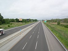 An overhead view of a divided highway with six lanes and a raised median barrier traveling through a rural area