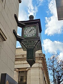 An exterior photo of a copper and stained glass clock projecting from the corner of a bank building