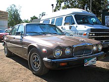 A picture of a Jaguar XJ sedan, parked in front of a van