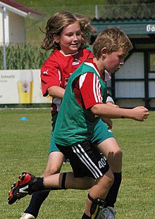 A boy and a girl chase a soccer ball