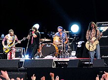 A photograph of four members of the Red Hot Chili Peppers performing on a stage