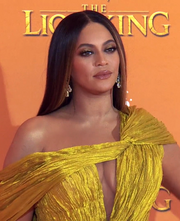 A black woman wearing a yellow dress poses for the camera in a red carpet