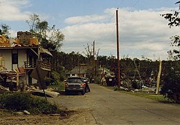 Cleared street with piles of refuse, scattered debris, and a damaged house nearby