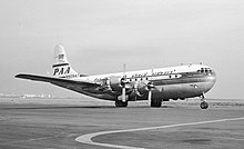 Vue de trois-quarts avant d'un avion de ligne à hélices ; la partie inférieure du fuselage est en métal nu, la partie supérieure est peinte en blanc et porte l'inscription « Pan American World Airways ».