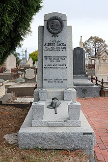 Albert Jacka's grave and headstone. A brass relief depicting a side view of Albert Jacka's head encircled by a wreath is on the headstone. A brass slouch hat and sword are attached to the top of the grave.