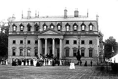 Photographie ancienne en noir et blanc d'un manoir néoclassique devant lequel une foule est réunie pour un évènement festif.