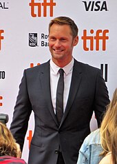 A man with blond hair and dressed in a black suit at a film premiere