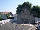 Photographie d’un fronton de pierres sur lequel s’affrontent au chistera six joueurs.