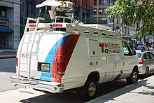 A white panel van with broadcasting equipment on the roof. The vehicle is wrapped in a design with blue and red accents and the Noticiero Telemundo 47 logo on the side.