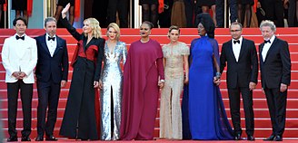 Photographie au format paysage et en couleurs de plusieurs personnes en tenue de gala, posant en souriant sur un tapis rouge.