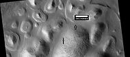Layers exposed at the base of a group of buttes in Mangala Valles in Memnonia quadrangle, as seen by HiRISE under HiWish program. Arrows point to boulders sitting in pits. The pits may have formed by winds, heat from the boulders melting ground ice, or some other process.