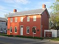 Small rectangular red brick house with white roof and many windows