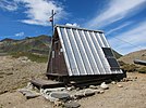 Petite cabane triangulaire dans un paysage montagneux.