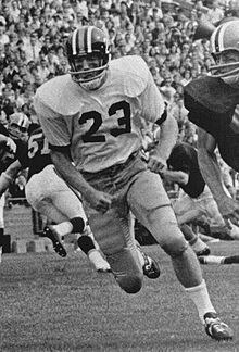 Roger Wehrli in a full uniform and helmet running on a football field.