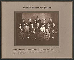 Photographie de groupe en noir et blanc représentant plusieurs femmes et hommes répartis en trois rangées. Plusieurs hommes portent des uniformes militaires.