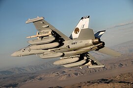 An EA-18G Growler, carrying under each wing an external fuel tank, a AN/ALQ-99 system with a ram air turbine, a jamming pod, and an AGM-88C HARM anti-radiation missile, with an additional AN/ALQ-99 system centered under the fuselage of the aircraft