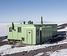 Cabane en taule verte devant la banquise et en fond un volcan.