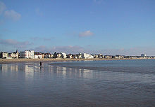 Photographie montrant une grande plage de sable fin de forme courbe à marée basse