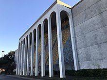 A large building with marble columns. A colorful, abstract mural is visible behind the columns.