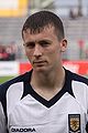 Head and shoulders of a young dark-haired white man wearing a football shirt with Scotland badge