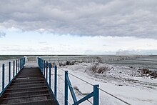 A long pier that curves right, with ice frozen along the entirety of the pier.