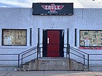 Grey stucco exterior with a red door. Black eagle shaped sign reads "Denver Eagle"