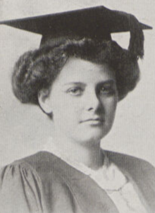 A young white woman with dark hair in a bouffant updo, wearing an academic cap and gown