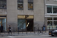 Looking east at the entrance to the 47th–50th Street–Rockefeller Center station inside 30 Rockefeller Plaza and NBC Studios from across Sixth Avenue. The entrance has gold trimmings and signs reading "Subway".