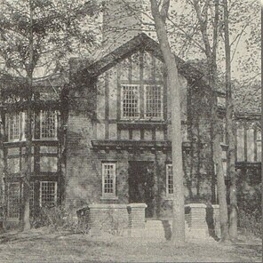 A two-story Tudor style building in a forest of tall trees