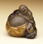 Hotei dreaming on his bag of treasures. Ceramic with gold and lacquer. Japan, mid-19th century.