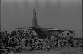 Troops from the 101st Airborne Division are pictured sitting in the grass at the Oxford airfield as a large military cargo aircraft unloads a Jeep