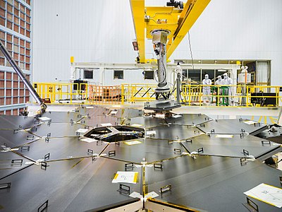 Primary mirror almost fully assembled (18/18 segments), with covers, robotic arm holding the last segment, February 2016