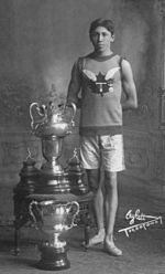 Young adult male wearing athletic running attire, standing beside two large trophies