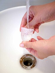 Rinsing a cup under cool, clean running water in a sink. Hot water speeds coagulation and can set bloodstains.