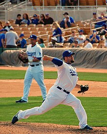 A man in a white baseball uniform and blue cap