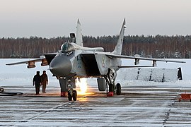 Un avion biréacteur sur une piste avec deux personnes à proximité ; en arrière-plan une forêt enneigée.