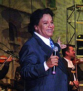 A man wearing dark blue tuxedo and tie is performing on stage