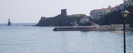 photographie couleurs : un port avec une jetée et en arrière plan une tour en ruines sur un promontoire