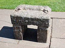A large grey stone with two rings attached, propped up on two smaller stones.