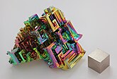 Bismuth in crystalline form, with a very thin oxidation layer, and a 1 cm3 bismuth cube