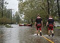 A photograph of two men walking on a flooded street towards a group of men in rafts in the background (from Tropical cyclone response)