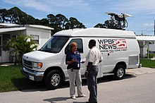 A reporter and official talking in front of a WPBF News 25 van