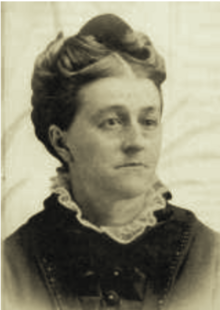 19th-century B&W portrait photo of a woman with her hair in an up-do, wearing a dark blouse with a frilly white collar.