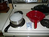 Kraft Macaroni & Cheese preparation—pot of boiling water with pasta inside, package of cheese powder (labeled "Kraft cheese sauce mix"), and colander to separate the noodles from the cooking water