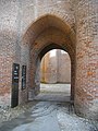 Photo couleur d'une porte à voûte en arc brisé en brique rouge. L'épaisseur des murs est visible, environ le double de la larguer de la porte.