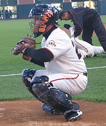 A man in a white baseball uniform and black catching gear