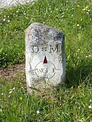 Photographie en couleurs d'une petite borne en pierre portant des inscriptions.