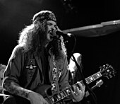 Der Stoner-Musiker Brant Bjork (links), hier in der Kantine in Augsburg, mit langen krausen Haar und Stirnband ist ebenso wie der positiv gestimmte Kirk Windstein (rechts), hier mit Crowbar beim Roadburn Festival, mit seinem rasierten Kopf und langen Bart, populäre Musiker wie Stereotype der Doom-Metal-Szene.