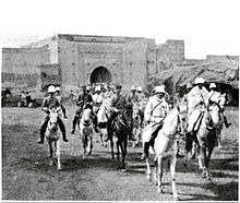 A photograph of General Mangin entering Marrakesh through a large gate at the head of a column of French horsemen